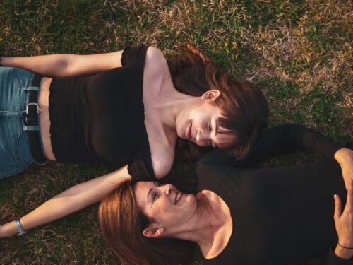 mother and teen daughter lying down on grass and talking